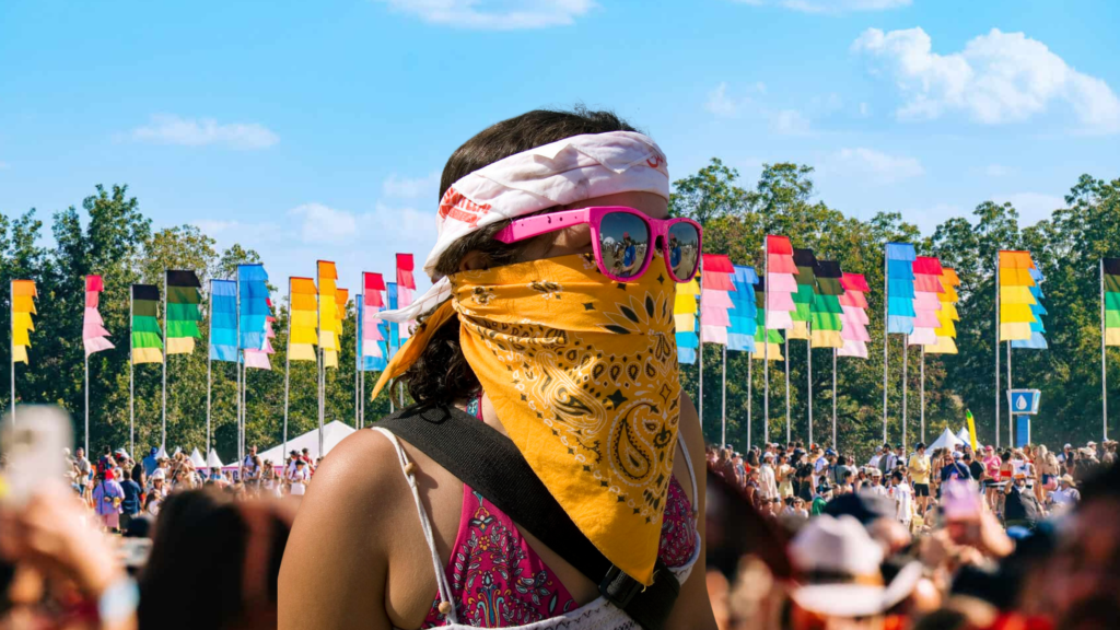 Asistente con bandana amarilla en el rostro y lentes rosas frente a las banderas de colores del ACL Festival 2026 en Zilker Park, Austin.